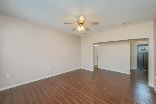 a view of an empty room with wooden floor and a ceiling fan