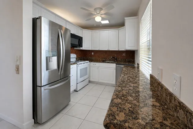 a kitchen with stainless steel appliances granite countertop a refrigerator a sink and white cabinets