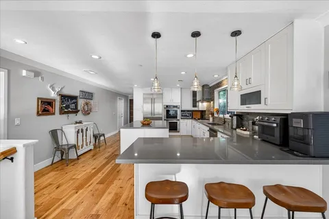 a kitchen with stainless steel appliances granite countertop a stove top oven a sink a dining table and chairs with white countertops