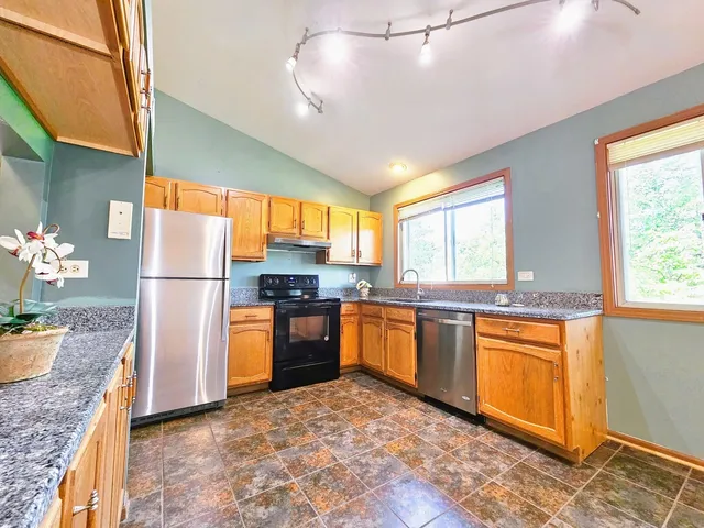 a kitchen with stainless steel appliances granite countertop a refrigerator a sink dishwasher a stove a dining table and chairs with wooden floor