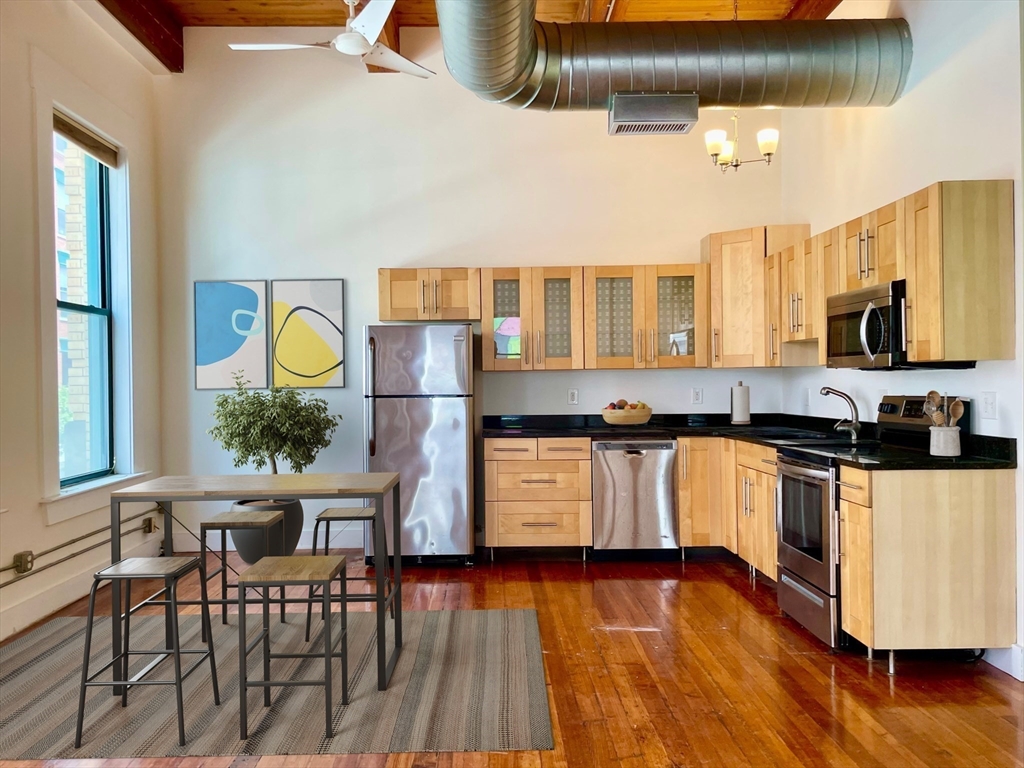 49 Munroe Street, Unit 201 Lynn, MA 01901 - Photo 2 of 16 a kitchen with stainless steel appliances granite countertop a stove a sink dishwasher a microwave oven and a dining table with wooden floor