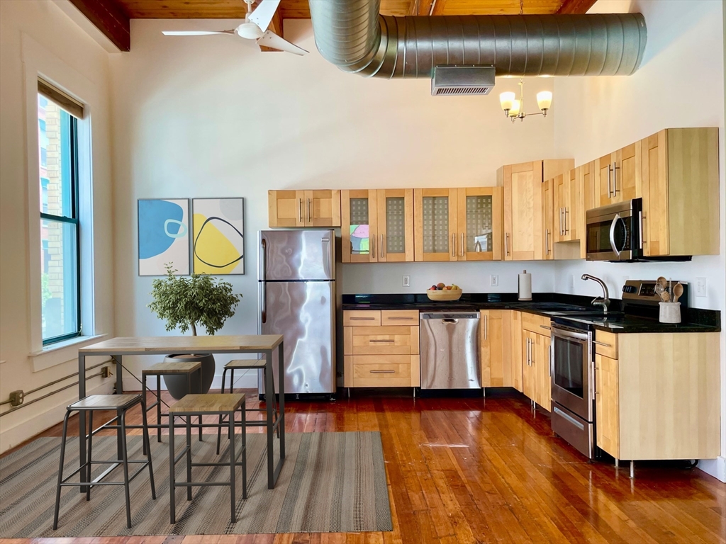 49 Munroe Street, Unit 201 Lynn, MA 01901 - Photo 3 of 16 a kitchen with stainless steel appliances granite countertop a stove a sink dishwasher a microwave oven and a dining table with wooden floor