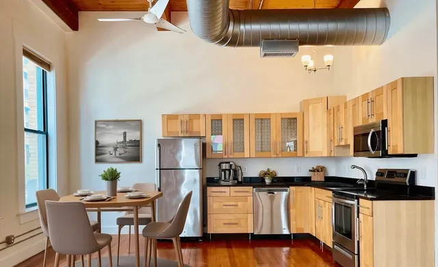 a kitchen with stainless steel appliances granite countertop a refrigerator a stove a sink a dining table and chairs with wooden floor