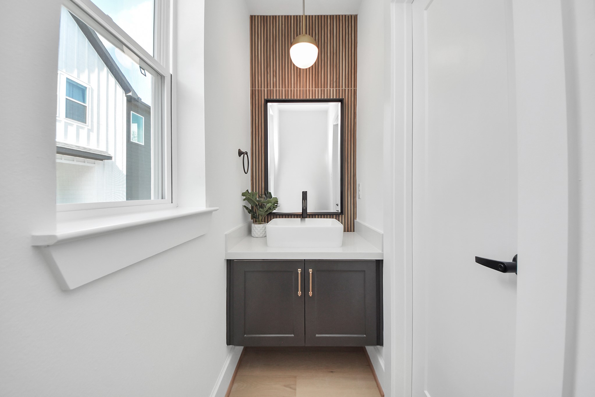 927 Fisher Street, Unit B Houston, TX 77018 - Photo 33 of 47 Step into this modern, compact bathroom featuring a sleek vanity with a white countertop and vessel sink. A stylish pendant light hangs above a wood-accent wall, while natural light from the window brightens the space, creating a clean and inviting design.