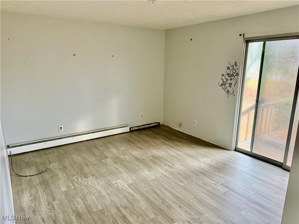 2898 Canton Road Uniontown, OH 44685 - Photo 14 of 20 Spare room featuring light wood-style floors, baseboard heating, and a textured ceiling