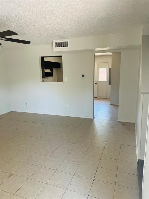 Spacious living area featuring neutral-toned tile flooring, a contemporary ceiling fan, and a pass-through window to the kitchen