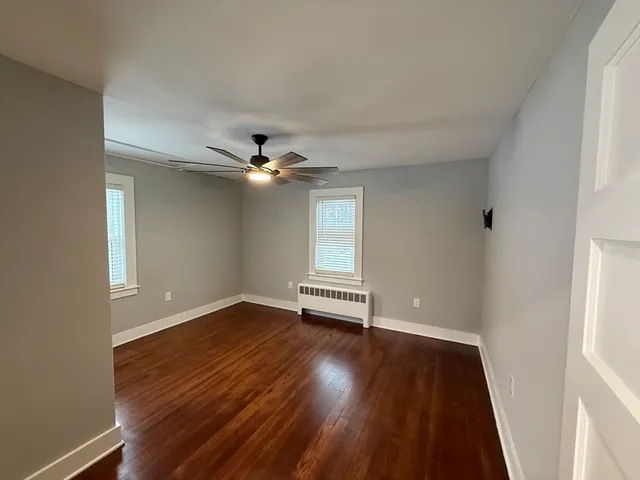 an empty room with wooden floor fan and windows
