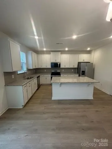 a large kitchen with stainless steel appliances granite countertop a stove a sink a refrigerator white cabinets and a granite countertops with wooden floor