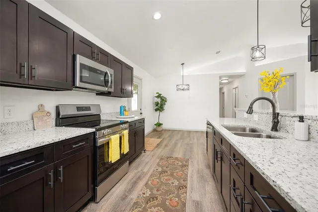 a kitchen with stainless steel appliances granite countertop a sink a stove top oven a refrigerator with wooden cabinets and floor