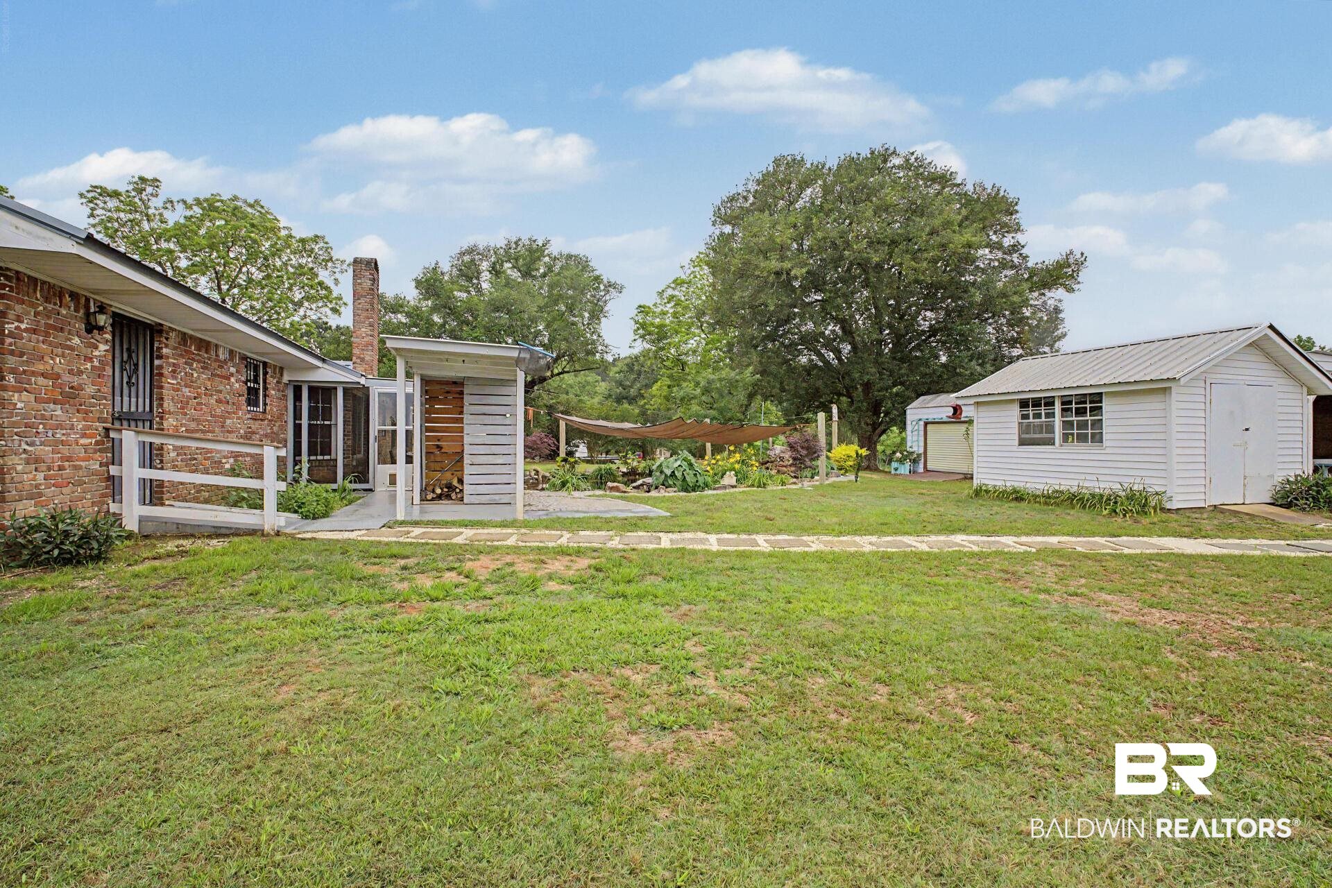 3791 Robinsonville Road Atmore, AL 36502 - Photo 12 of 47 Expansive backyard featuring a brick exterior structure, a white detached shed with a metal roof, a covered outdoor storage area, a paved patio, and a garden area with raised beds