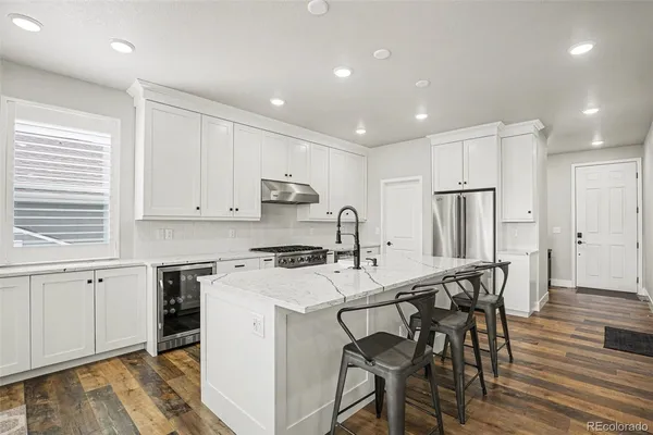 a kitchen with stainless steel appliances a stove a sink a refrigerator white cabinets and wooden floor