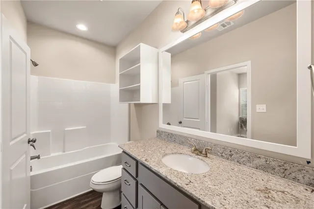 a bathroom with a granite countertop sink a toilet a mirror and bathtub