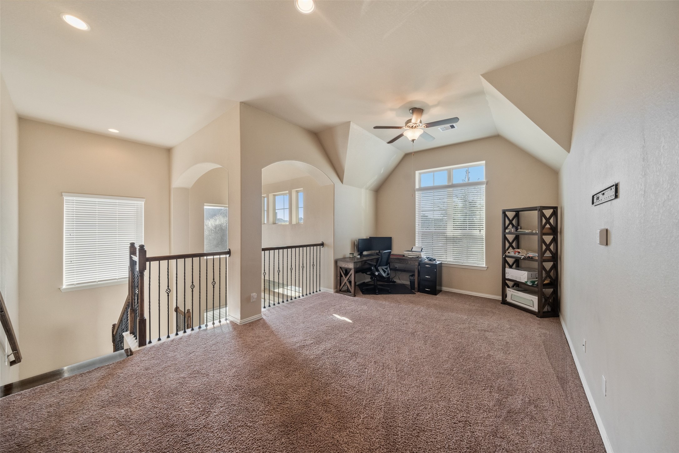 4747 Abercorn Street Rosharon, TX 77583 - Photo 24 of 46 This spacious upstairs area features soft carpeting, ample natural light from large windows, and a ceiling fan. It includes an open space ideal for a home office or cozy sitting area, with a stylish railing overlooking the lower floor.