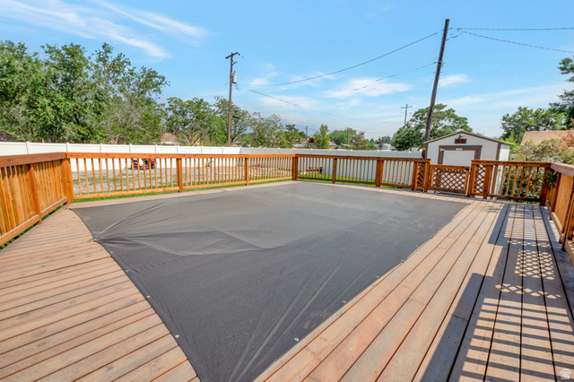 7391 Elm Street Midvale, UT 84047 - Photo 27 of 38 Expansive wooden deck surrounding a covered pool, featuring a perimeter wooden fence and an outdoor storage shed