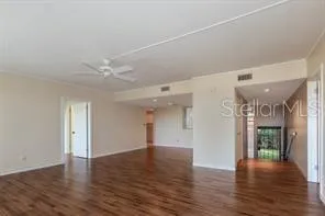 a view of an empty room with wooden floor and a ceiling fan