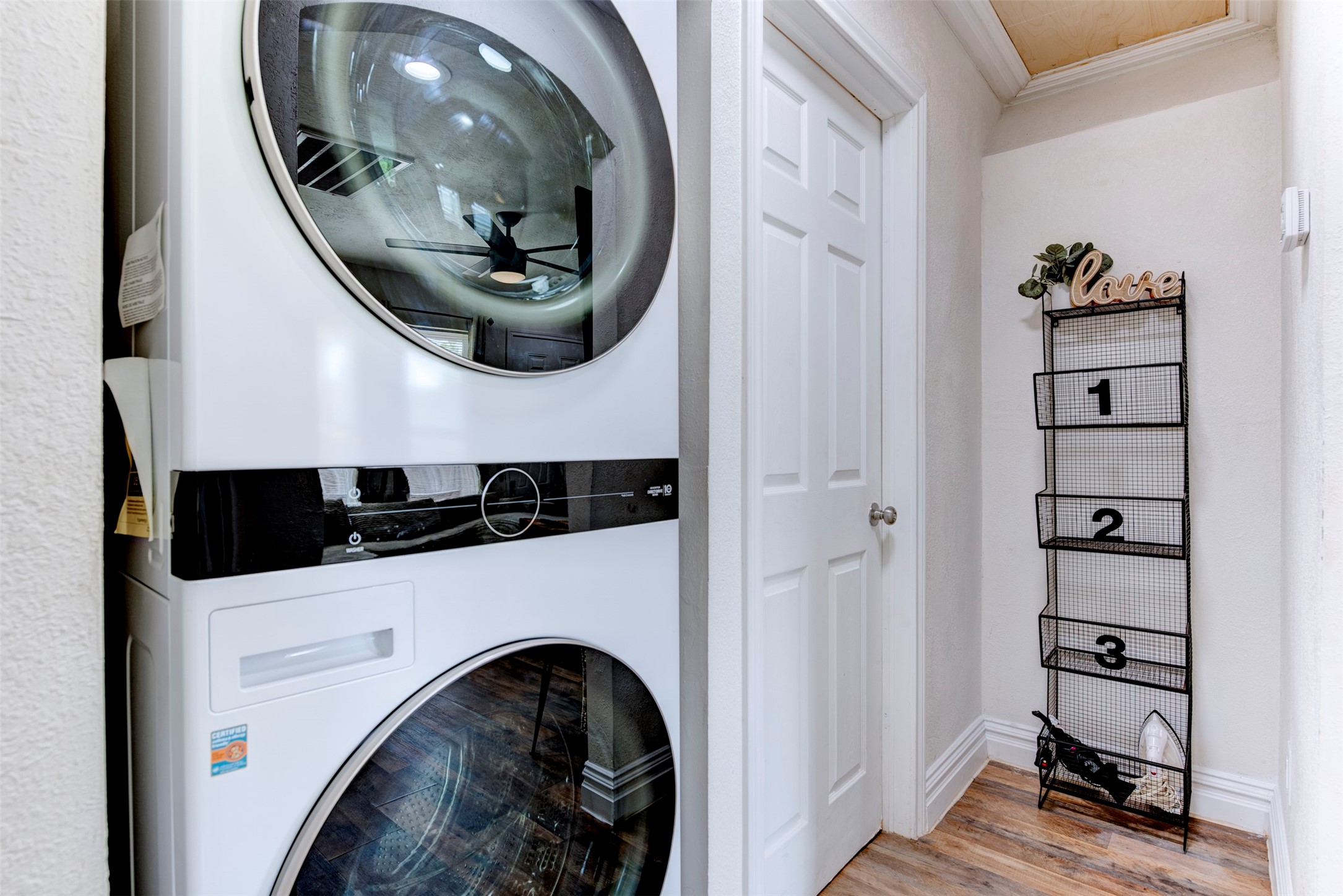 1121 Panama Street Houston, TX 77009 - Photo 28 of 35 In-unit hallway laundry closet featuring full-size stacked front-load washer and dryer with black control panel accents, six-panel interior door, wood-look LVP flooring, and wood plank ceiling detail.