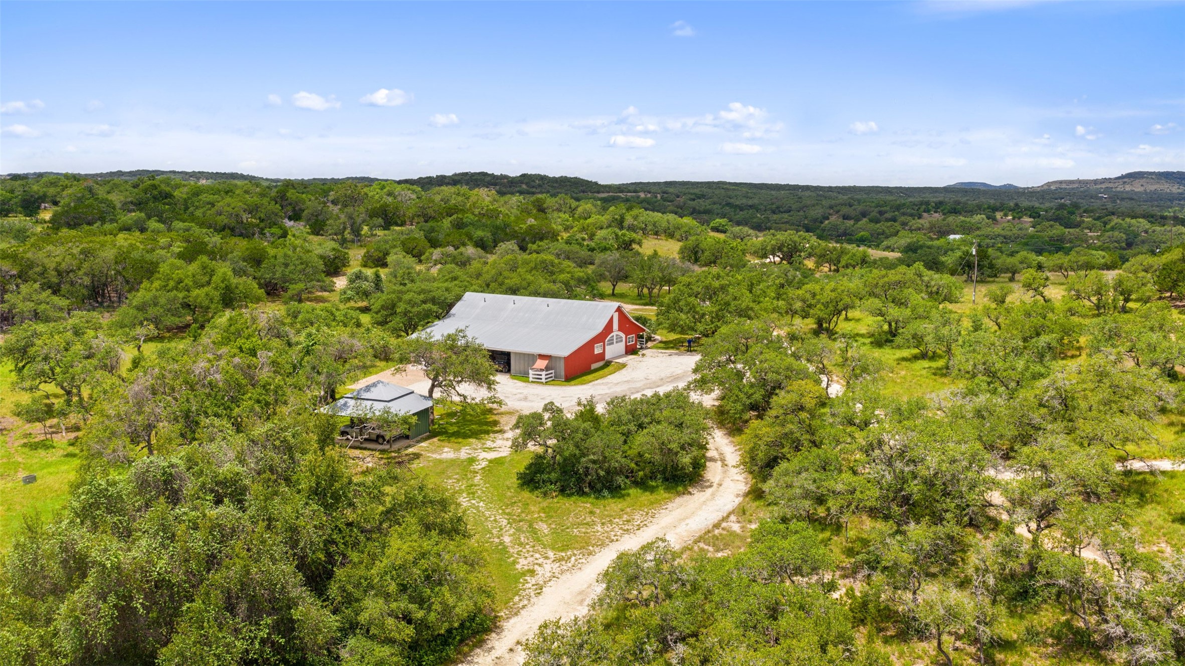 505 Red Corral Ranch Road Wimberley, TX 78676 - Photo 6 of 40 A picturesque red barn stands amidst sprawling green trees, offering a serene rural escape.