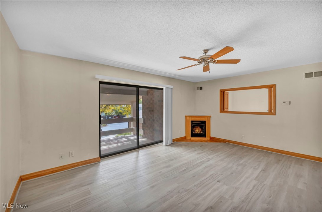 1263 Lost Nation Road, Unit 5 Willoughby, OH 44094 - Photo 8 of 26 Unfurnished living room featuring a textured ceiling, ceiling fan, light wood finished floors, and a lit fireplace
