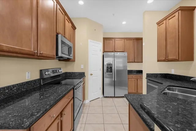 a kitchen with stainless steel appliances granite countertop a refrigerator a stove and a sink with wooden cabinets