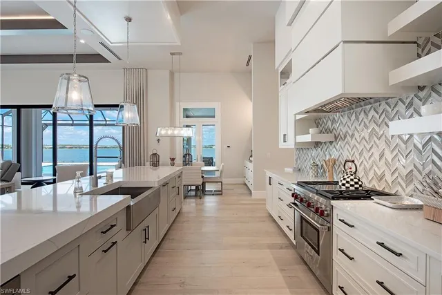 a large kitchen with stainless steel appliances a sink dishwasher a stove and a dining table with the view of living room