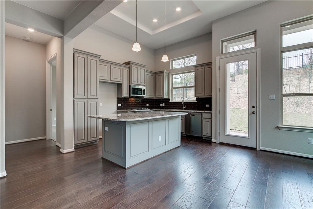 113 Cartwheel Bend, Unit 46 Austin, TX 78738 - Photo 3 of 10 Kitchen with gray cabinetry, a center island, decorative light fixtures, dark wood-style floors, and a tray ceiling