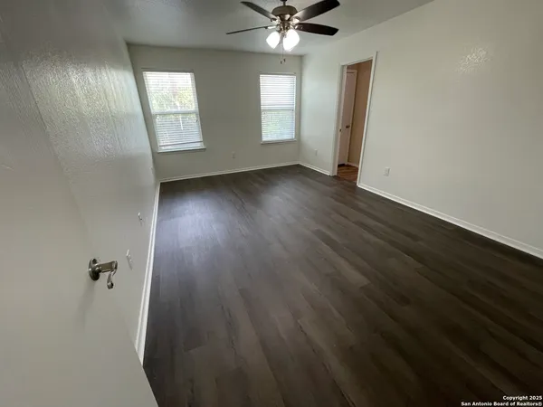 an empty room with wooden floor fan and windows