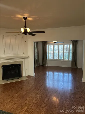 a view of an empty room with wooden floor fireplace and a window