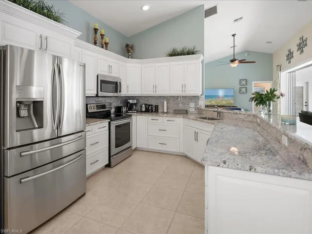 a kitchen with stainless steel appliances granite countertop a sink a stove a refrigerator and white cabinets