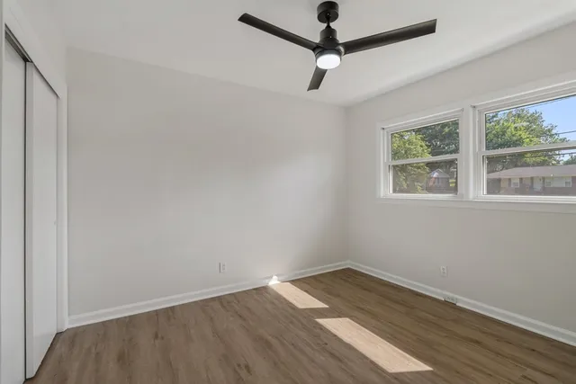 an empty room with wooden floor ceiling fan and windows