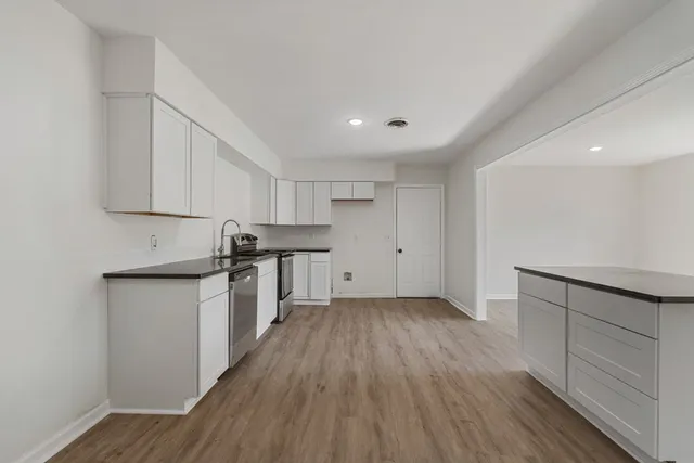 a kitchen with granite countertop a stove top oven a sink and white cabinets with wooden floor