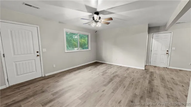 an empty room with wooden floor chandelier fan and windows