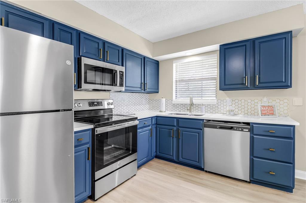 Kitchen with stainless steel appliances, blue cabinets, light wood-type flooring, tasteful backsplash, and a textured ceiling