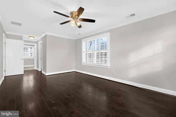 an empty room with wooden floor fan and windows