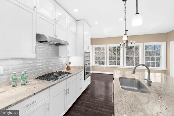 a kitchen with granite countertop a stove a sink a refrigerator wooden floor and cabinets