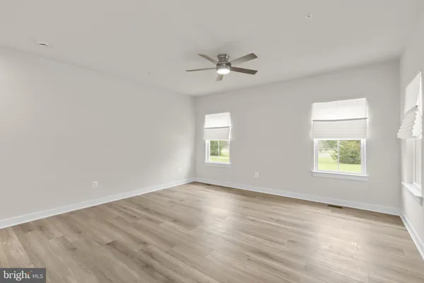 an empty room with wooden floor ceiling fan and windows