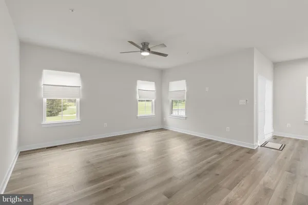 an empty room with wooden floor ceiling fan and windows