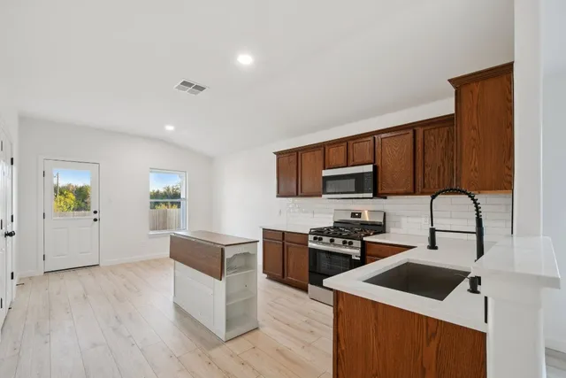 a kitchen with stainless steel appliances a stove a sink a microwave a refrigerator and cabinets