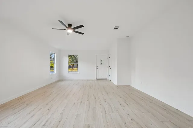 an empty room with wooden floor chandelier fan and windows