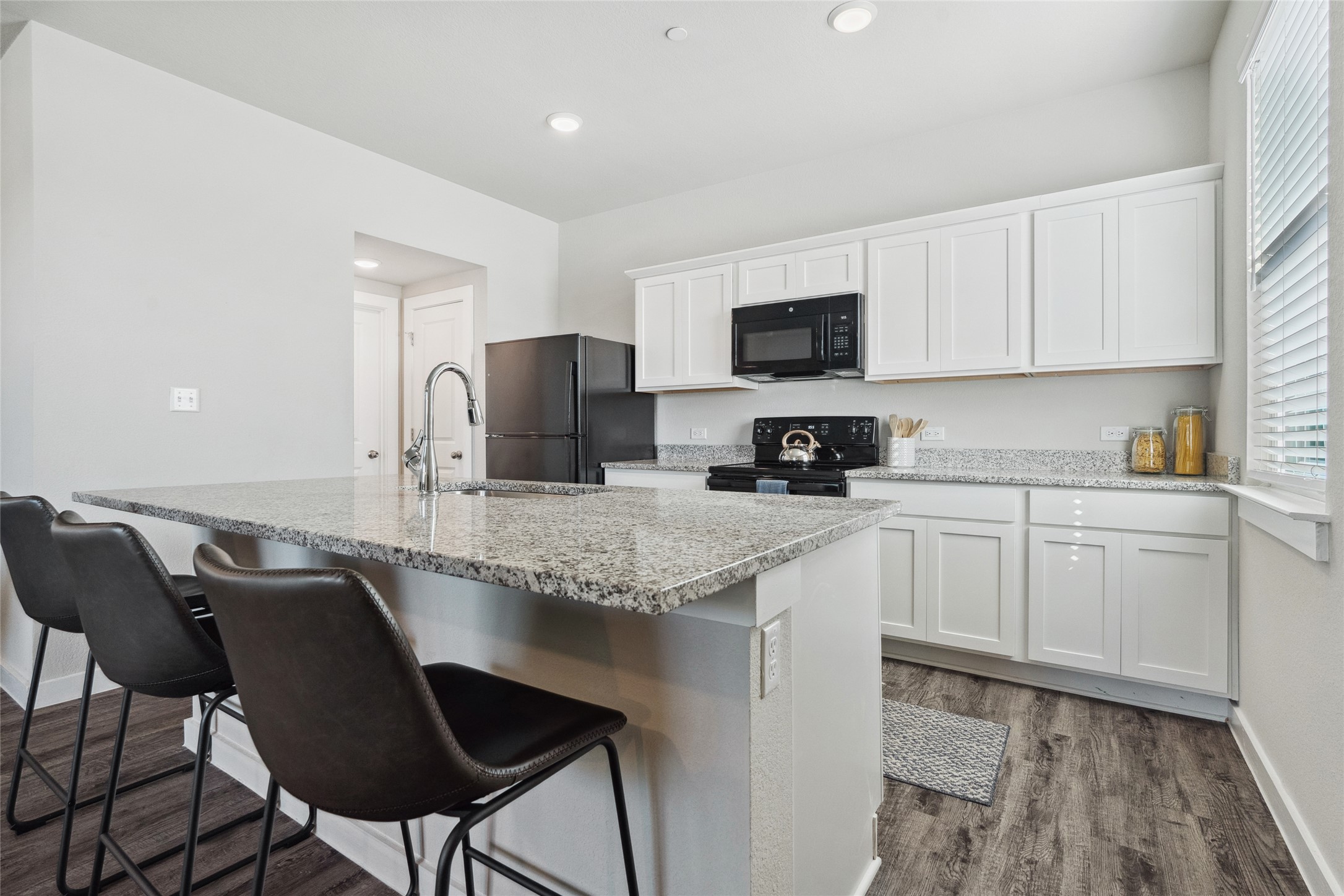 523 Powell Drive, Unit 1101 Leander, TX 78641 - Photo 8 of 24 Kitchen with white cabinetry, black appliances, an island with sink, a breakfast bar, and light stone countertops