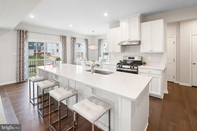 a kitchen with stainless steel appliances a stove a sink a refrigerator white cabinets and wooden floor