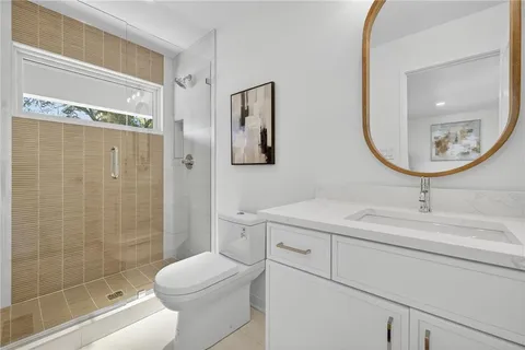 a bathroom with a toilet sink vanity granite and shower