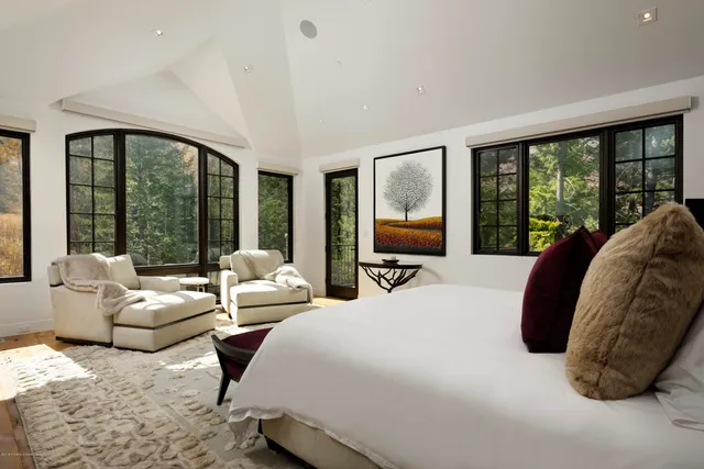 a bedroom with a bed couches and large windows
