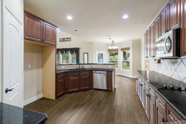 a kitchen with stainless steel appliances kitchen island granite countertop a refrigerator a stove top oven and a sink with wooden floor