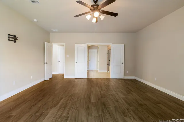 a view of an empty room with chandelier fan and wooden floor