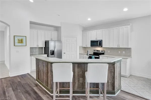 a kitchen with stainless steel appliances granite countertop a stove a sink a microwave a refrigerator and white cabinets with wooden floor