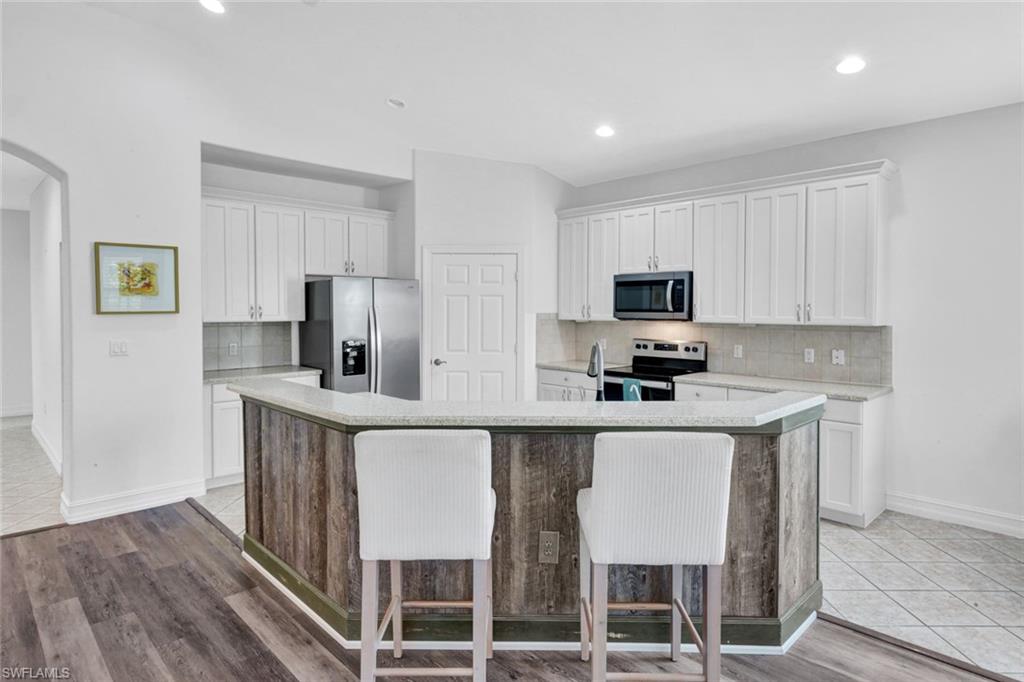 1277 Rialto Way, Unit 201 Naples, FL 34114 - Photo 9 of 46 a kitchen with stainless steel appliances granite countertop a stove a sink a microwave a refrigerator and white cabinets with wooden floor