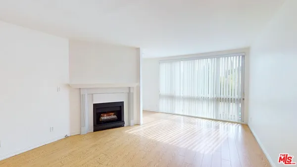 a view of an empty room with wooden floor fireplace and a window