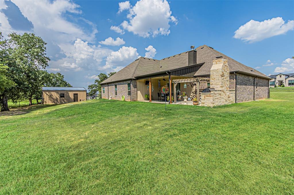 1009 Henry Way Springtown, TX 76082 - Photo 37 of 40 Rear view of property with a chimney, a patio, a lawn, board and batten siding, and an outdoor structure