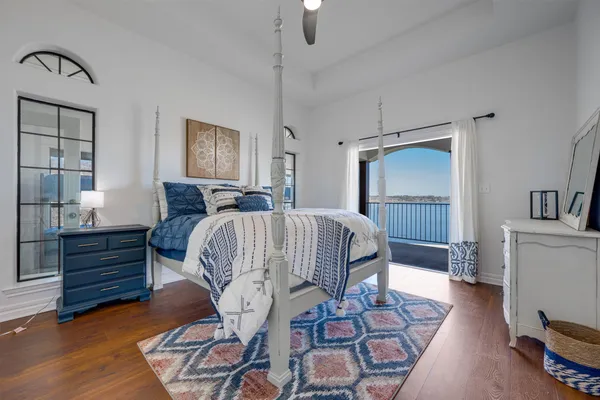 a bedroom with a bed and a lamp on dresser with wooden floor