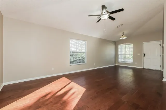 an empty room with wooden floor ceiling fan and windows